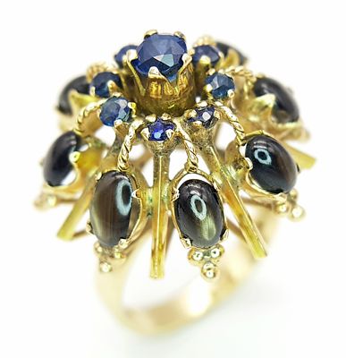 A 14K Yellow Gold Sapphire Burst Ring. Eight black star oval sapphires in surround form of