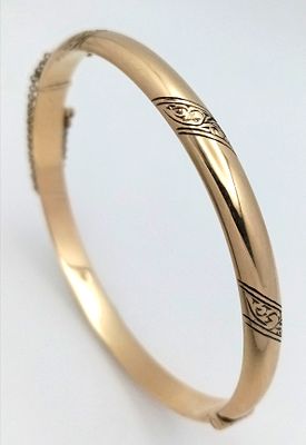 A 9K Yellow Gold Bangle. Clip open design. Safety chain. 7mm width. 9.75g.