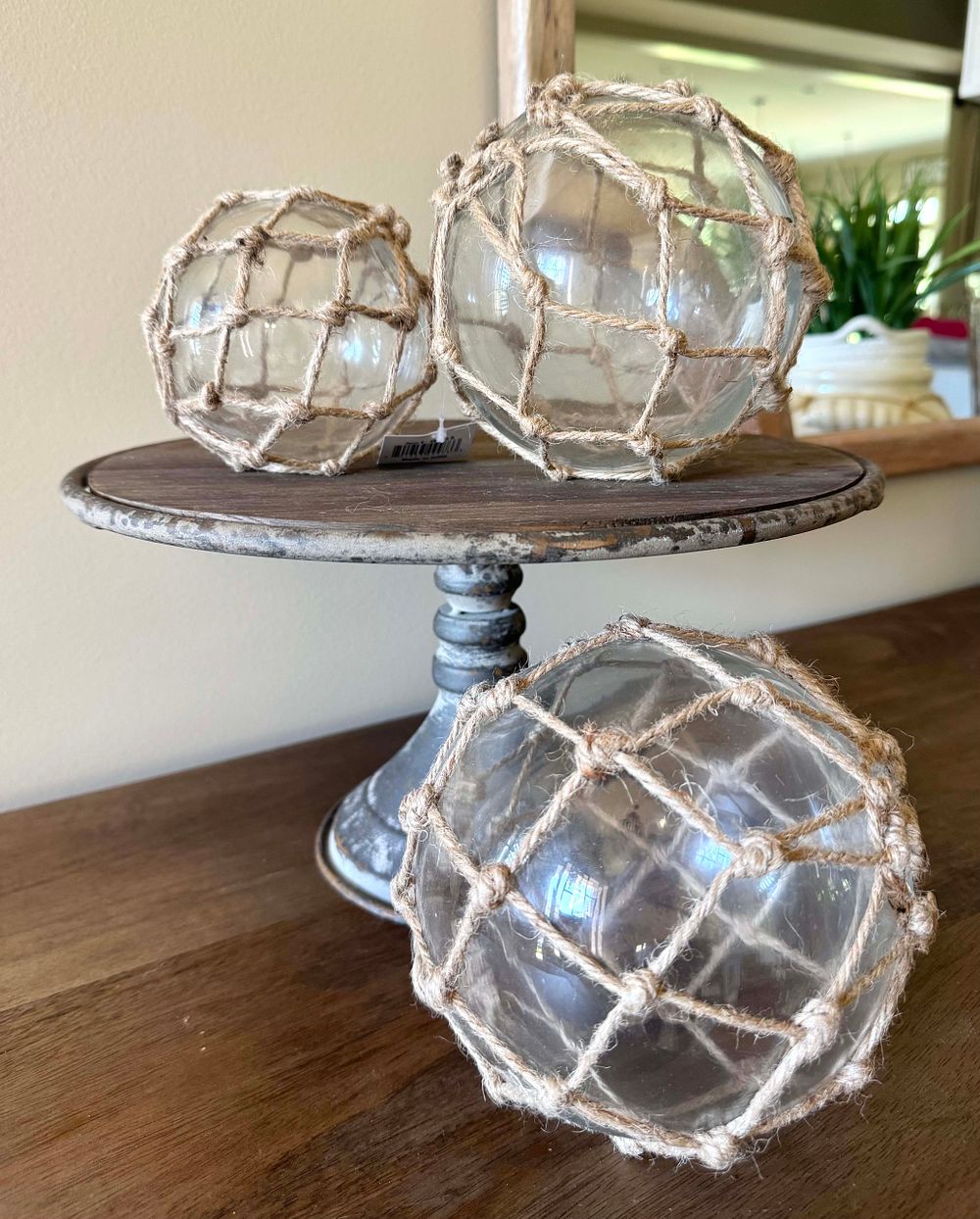 A Metal Cake Stand with Three Decorative Nautical-Style Glass Balls in Netting. This lot 