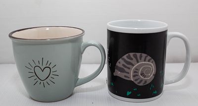 צמד ספלי קפה עם איורים שובי לב: ספל תכלת בעיטור "לב קורן" וספל שחור בעיטור חילזון ישן, לרגעים 