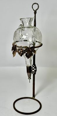 מעמד ברזל עם דקנטר קריסטל עם מנגנון מזיגה בחלק התחתון מעוטר ענבים וגפנים, גם בקריסטל וגם במתכת. 