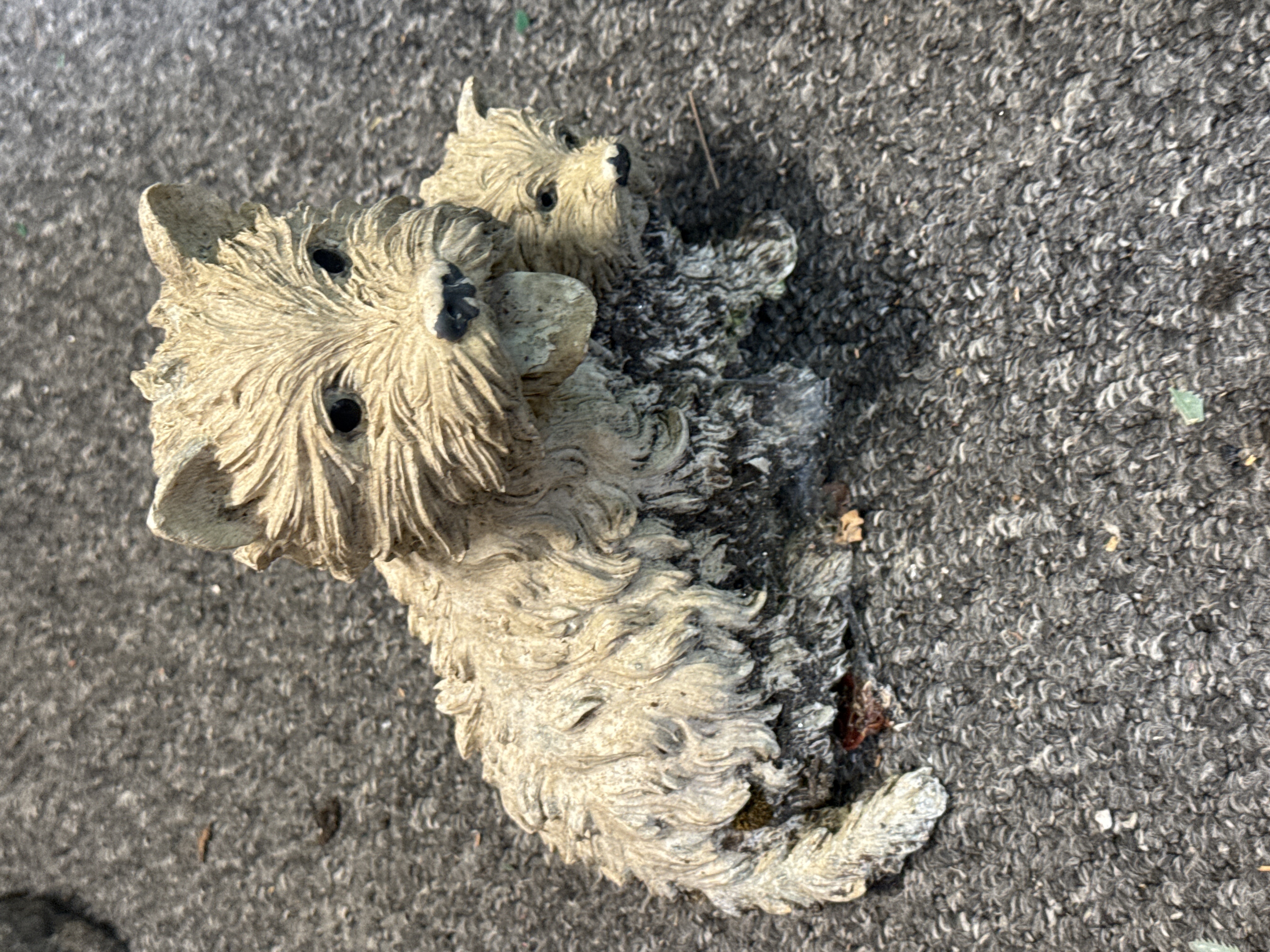 A weathered cast stone garden ornament of two Westie puppies