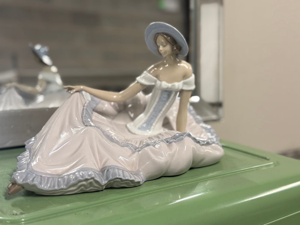 Lot 13: A NAO glazed porcelain figurine of a seated woman in a ruffled dress