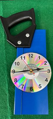 An Upcycled CD Clock and an Accompanying Hand Saw. This lot comprises an upcycled clock 