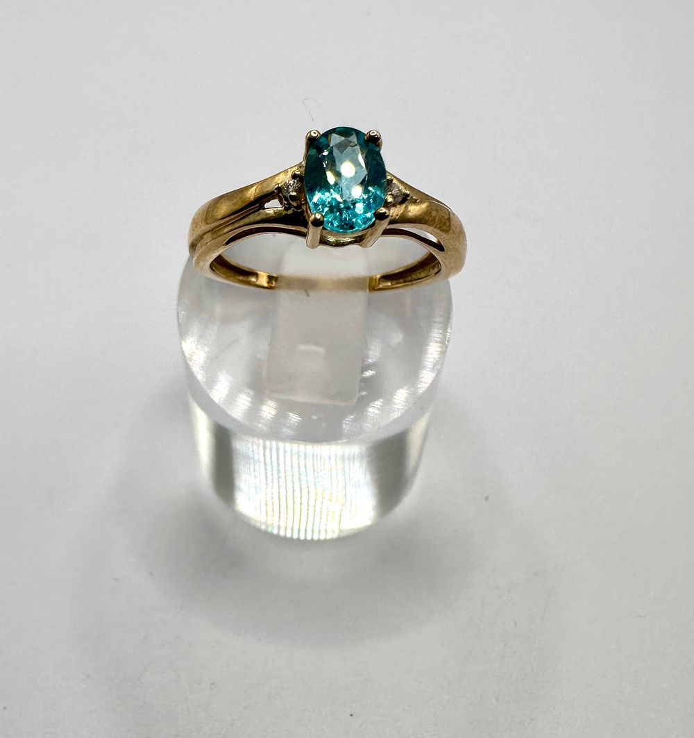 Lot 147: A 9 carat yellow gold dress ring set with an oval teal gemstone and colourless accent stones