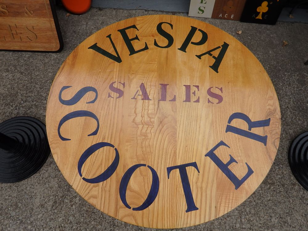 Lot 237: A circular wooden pedestal bistro table with Vespa Sales Scooter branding