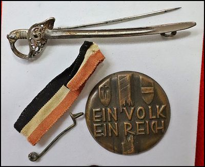 Lot of 2 German badges. (1) Sword-form stickpin, silvered metal, the blade inscribed AUS 