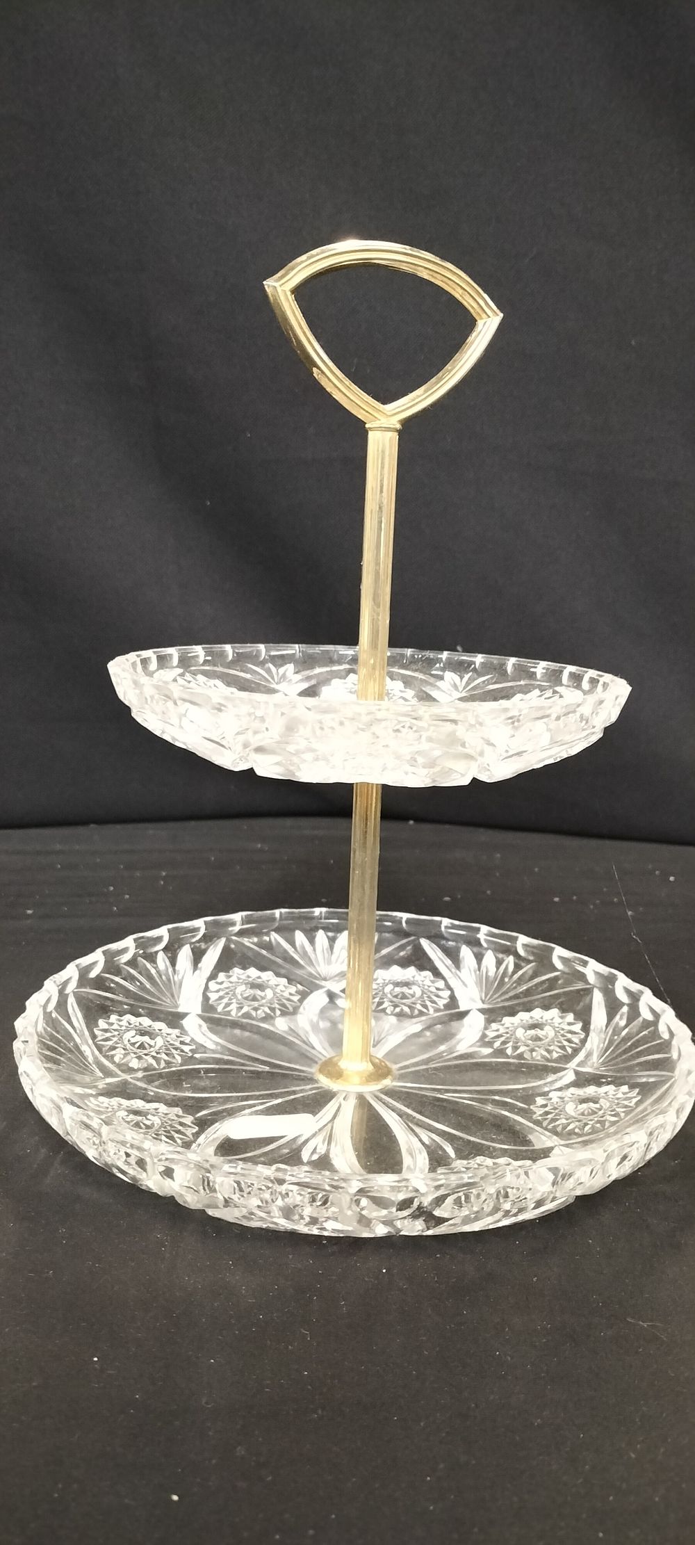 Lot 295: ** Cut-Glass Two-Tier Serving Stand with Gold-Tone Handle
**Detailed Description:** A clear, cut-glass two-tier serving stand with a gold-colored metal handle.
**Condition Report:** Good
**Estimated Value:** 30 - 50