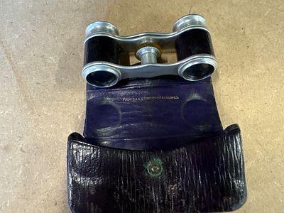 A pair of black and silver tone opera glasses with a central adjustment wheel, housed in a 