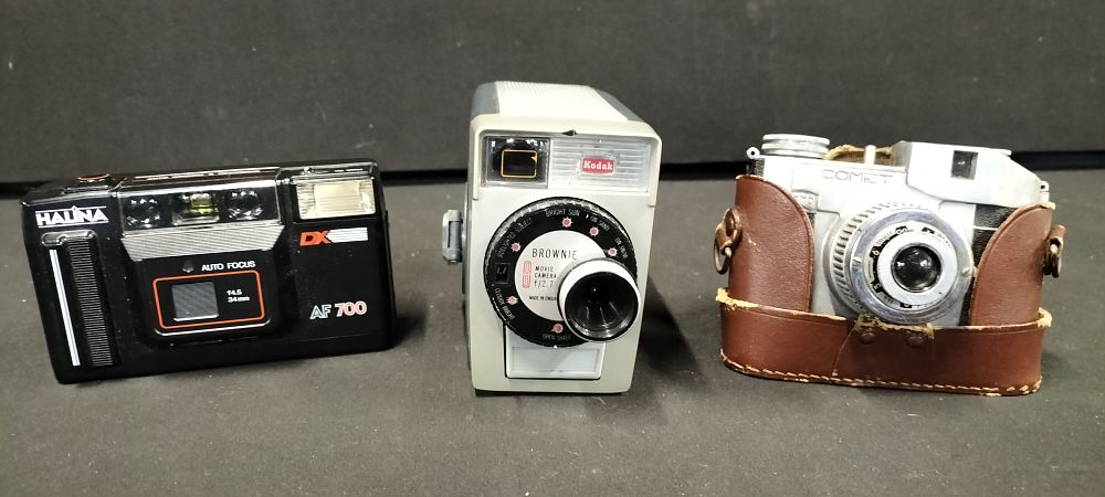 Lot 295: Three cameras comprising a black Halina AF 700 autofocus unit, a grey Kodak Brownie 8mm movie camera f/2.7, and a silver Comet 127 camera in a brown leather case.