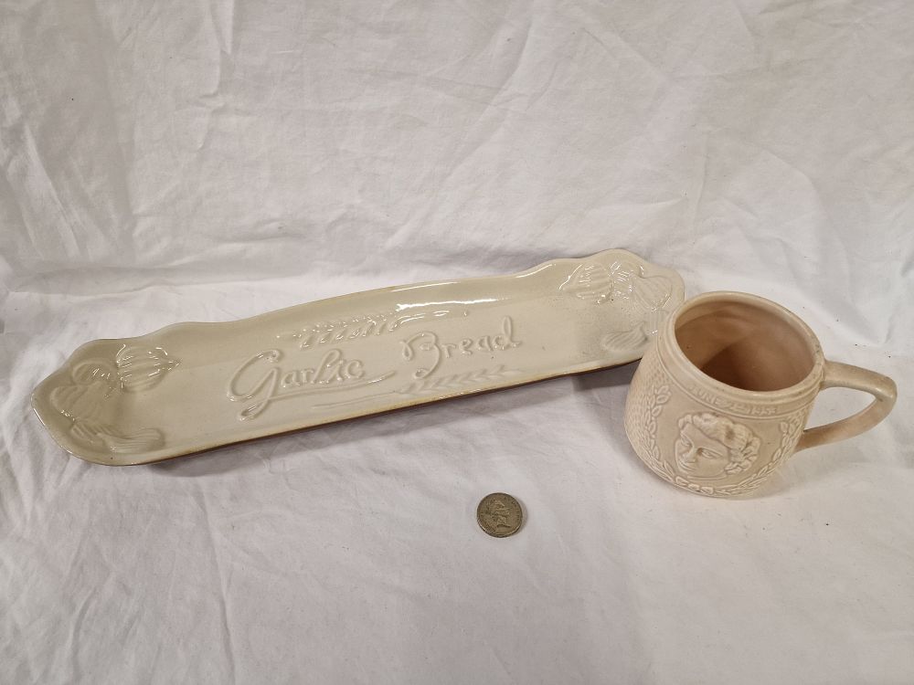 Lot 455: Two items of cream-glazed earthenware comprising a 1953 coronation mug and a French garlic bread serving tray