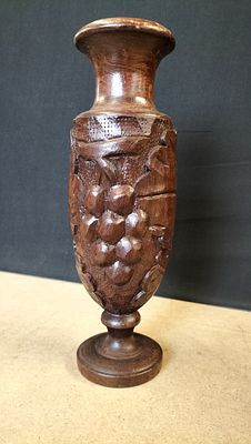 Hand-carved wooden vase with grape and leaf motif. A dark brown hand-carved wooden vase 