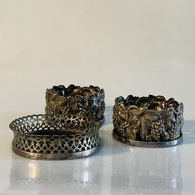 Duas bases de copos e uma de garrafa. duas bases de copos em metal prateado, relevado com parras 
