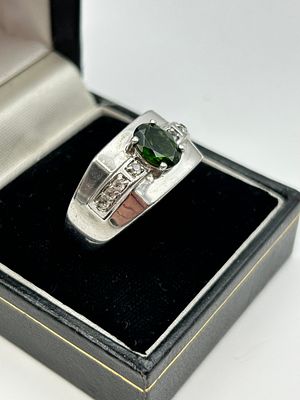 A silver dress ring set with an oval-cut green gemstone and diamond accents