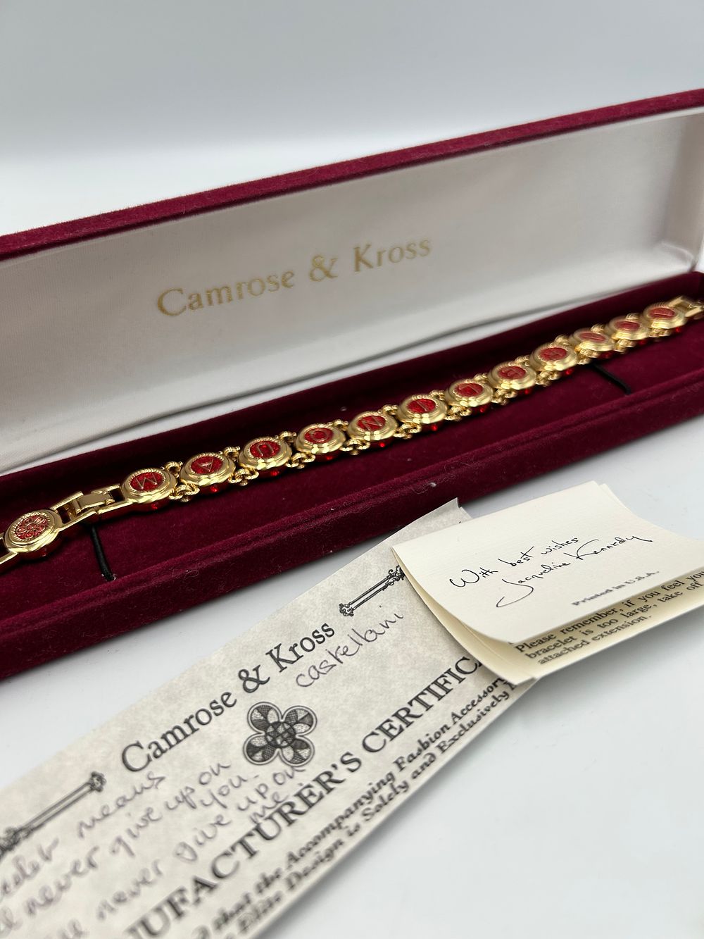 Lot 199: Camrose & Kross Gilt Metal Effect and Red Crystal Non Relinquam Bracelet