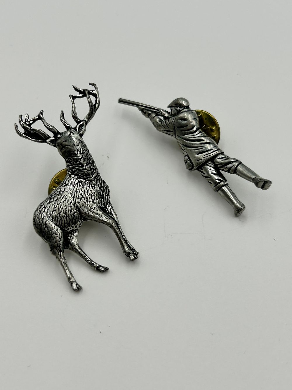 Lot 250: Two White Metal Lapel Pins Depicting a Prone Hunter and a Stag by Brown?
