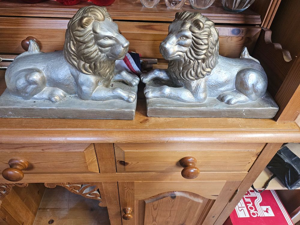 Lot 181 – A pair of mid-20th century silver and gold toned couchant lion figurines
