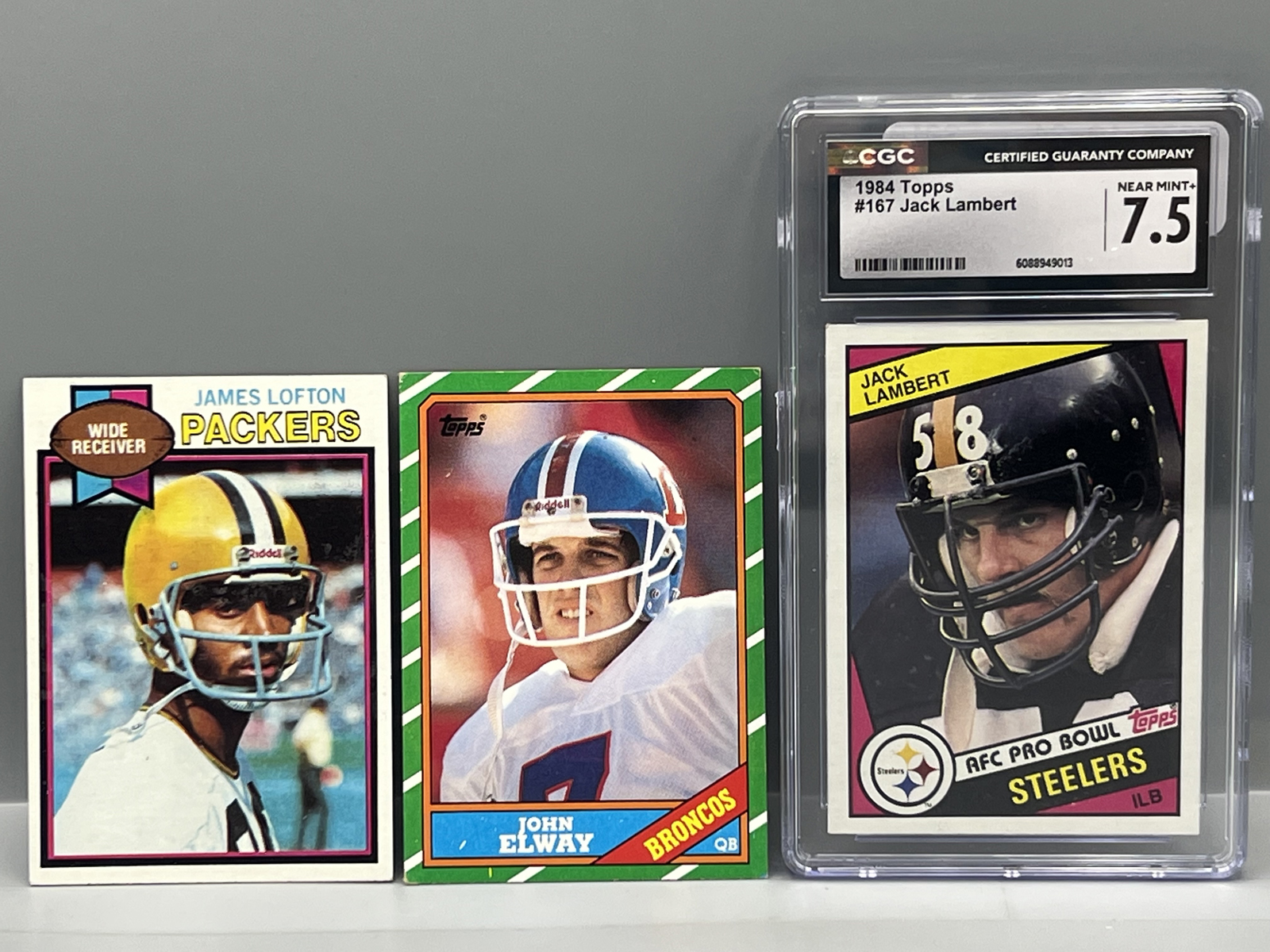 1979 Topps James Lofton RC #310, 1986 Topps John Elway #112, & 1984 Topps Jack Lambert #167 CGC NM+ 7.5