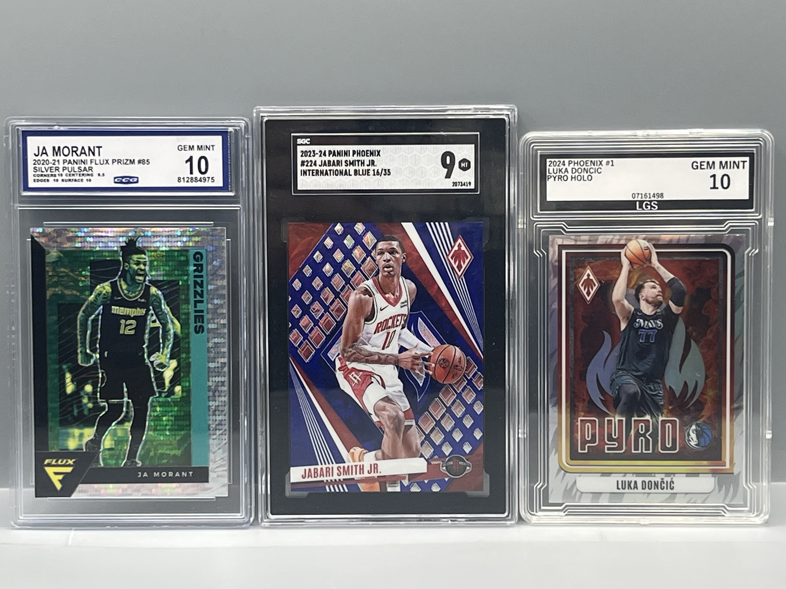 2020-21 Panini Flux Ja Morant Pulsar, 2023-24 Panini Phoenix Jabari Smith Blue #/35 SGC 9, & 2024 Panini Phoenix Luka Doncic Pyro #1