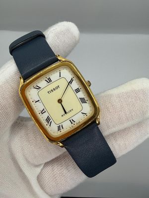 שעון מהמם של חברת Tissot בעיצוב רטרו עם גוף בצבע זהב, לוח לבן ושמנת , על הלוח רשום דגם Stylist 