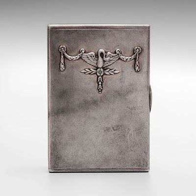 Портсигар с накладкой в виде геральдического знака из гирлянд лент и растений и лебедем в центре. 