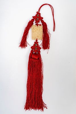 Placchetta in giada traforata raffigurante un cane di Fo, con nappe rosse. Cina, secolo XX cm 