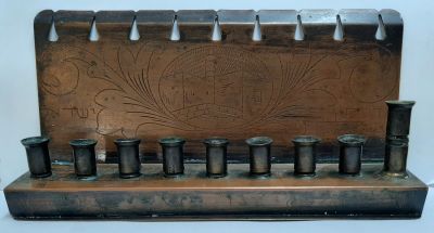 חנוכיה ראשית שנות ה-50 עם עבודת חריטה של מגדל דוד וכיתוב "מדינת ישראל" עשויה נחושת.
מידות: 22X12 ס"מ