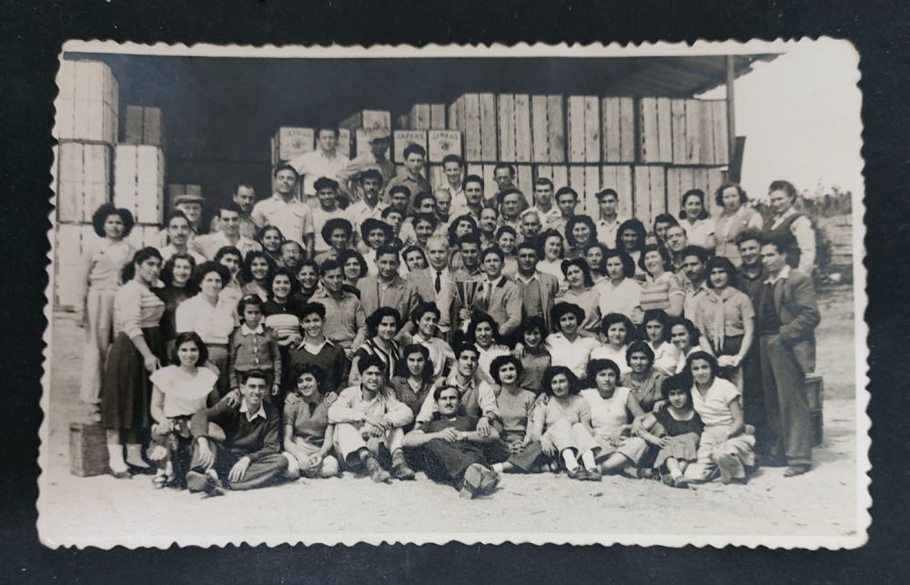 צילום מעניין בבית אריזה לפירות הדר בארץ ישראל. באמצע מישהו מחזיק גביע. אין לנו מידע לגבי האירוע