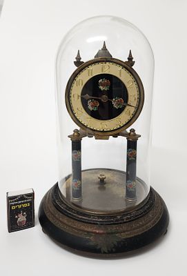 שעון גרמני מכני עתיק עם חוגת אמייל פרחונית תחת כיפה שקופה עשויה זכוכית – גרמניה ראשית המאה ה-20. 