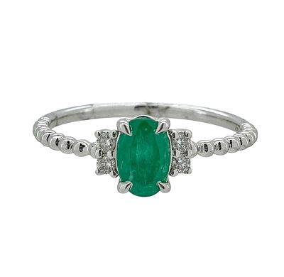 A classic and delicate 14K gold ring set with an emerald gemstone and flanked by natural white