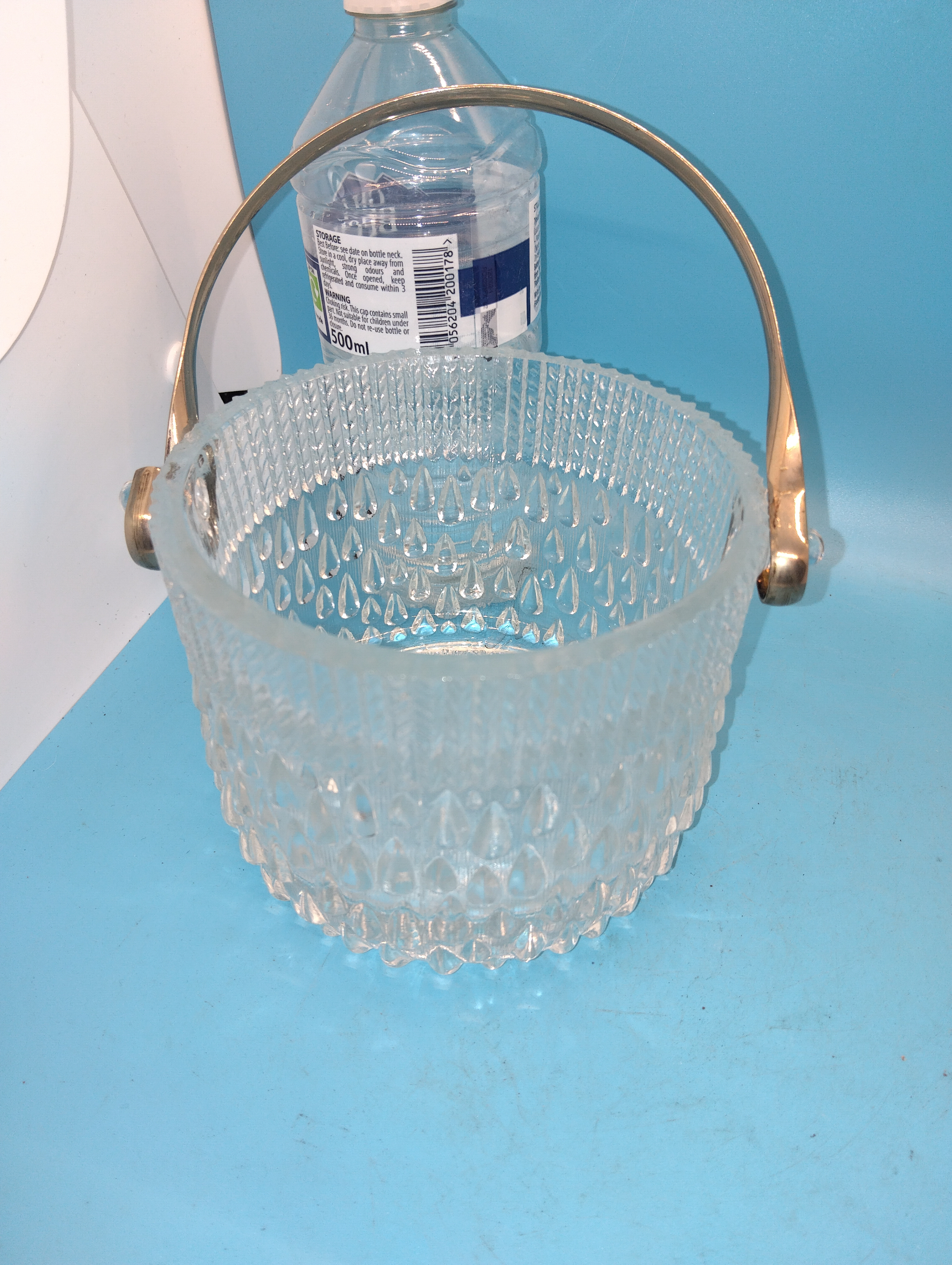 A mid-20th-century pressed glass ice bucket with metal swing-handle