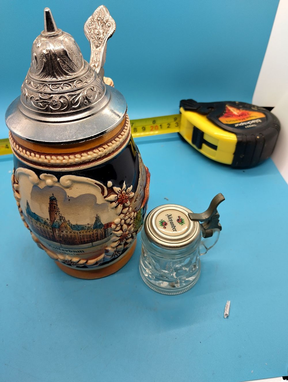 Two Souvenir Lidded Beer Steins comprising a Ceramic Rotterdam Example and a Miniature Glass Stein