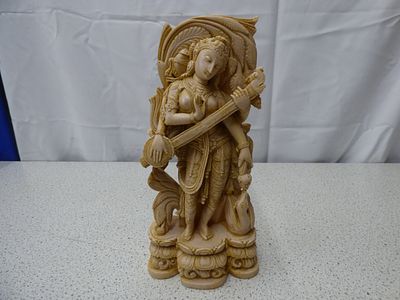 A Creamy Beige Saraswati Goddess Statue Playing Veena. A creamy beige or ivory-coloured statue 
