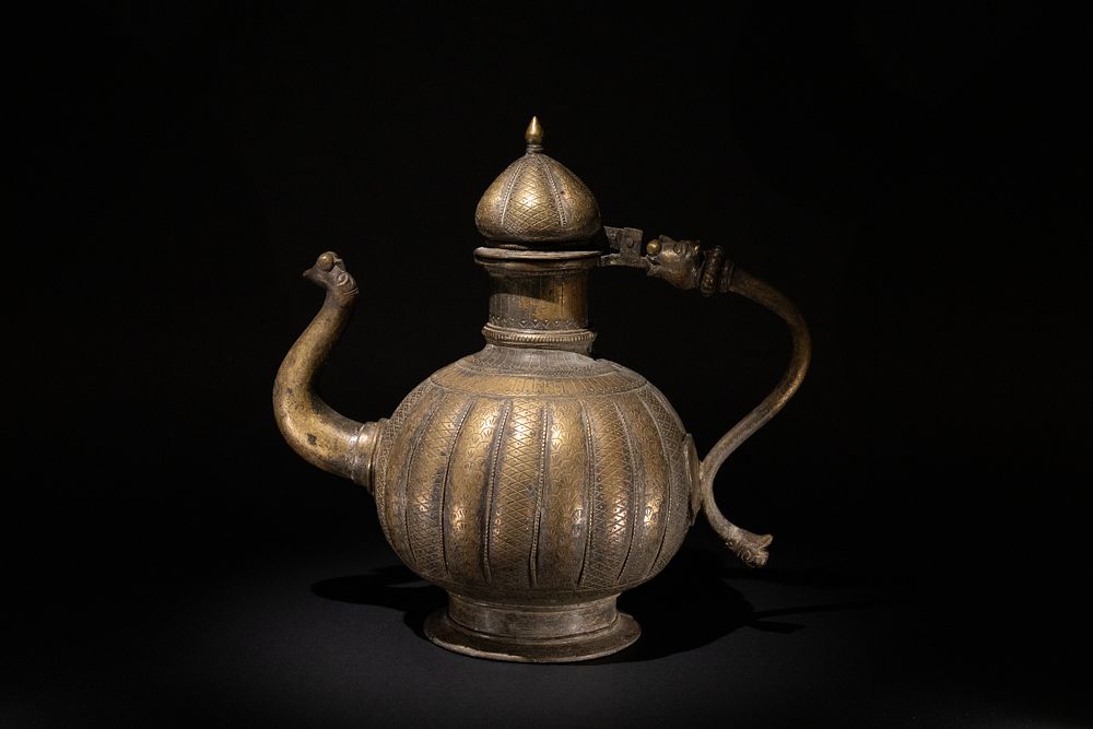 Lot 219: An Indian Mughal Brass Engraved Ribbed Ewer, 17-18th...