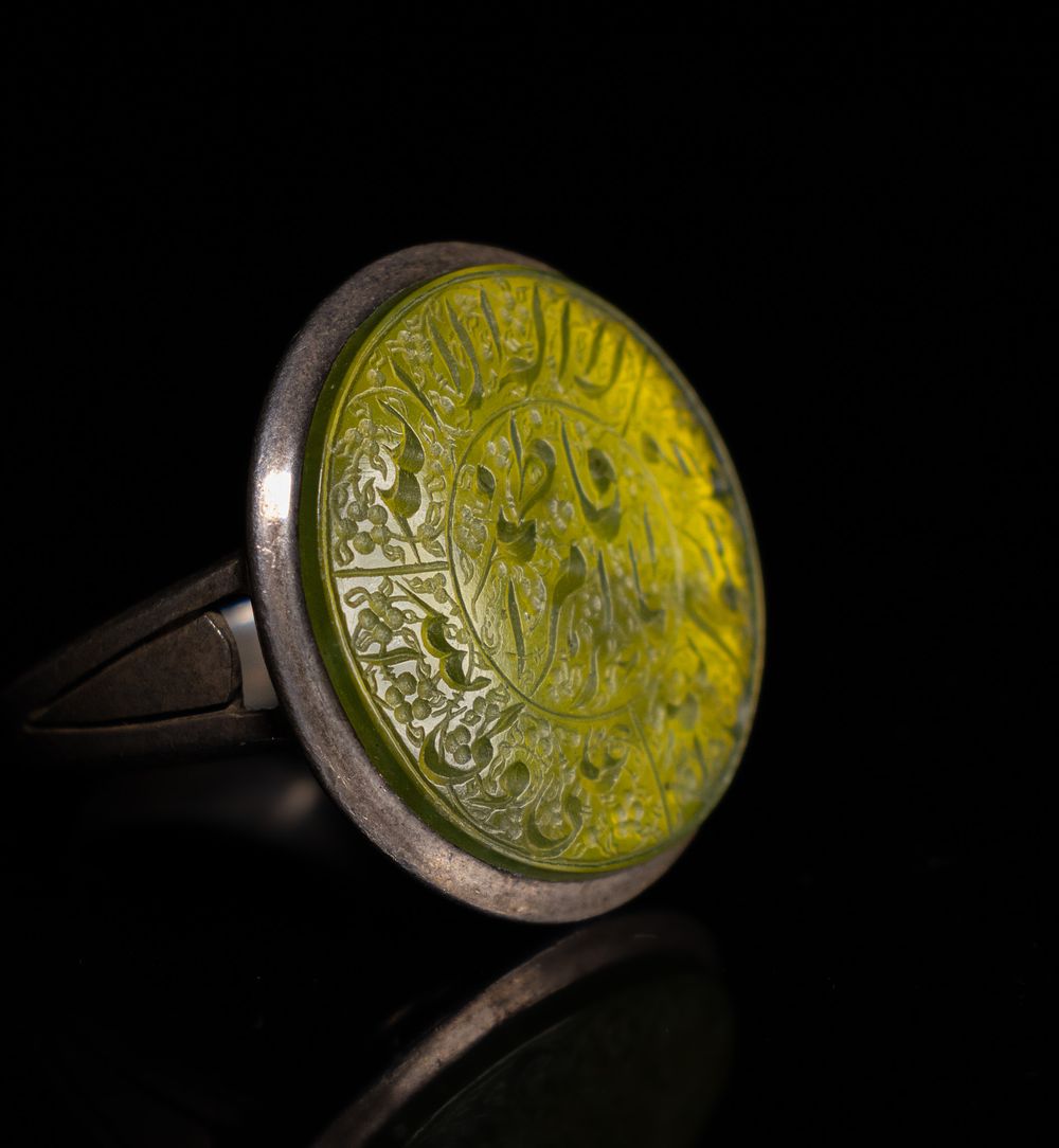 Lot 29: AN ISLAMIC SILVER TALISMANIC RING WITH CALLIGRAPHIC YELLOW AGATE INTAGLIO.