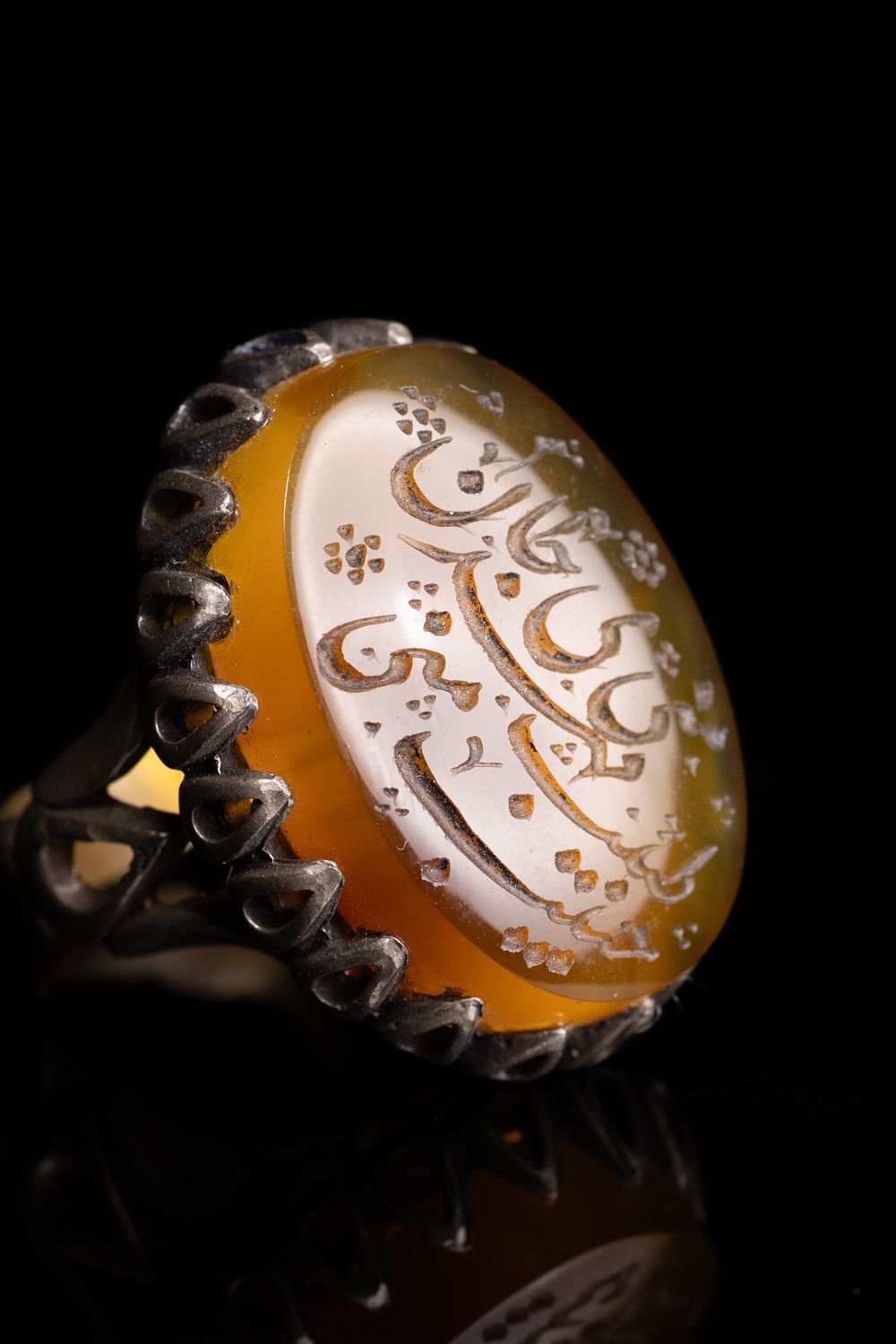 Lot 140: AN ISLAMIC YELLOW CARNELIAN AGATE SIGNET RING WITH ARABIC CALLIGRAPHY IN AN OPENWORK SILVER SETTING.