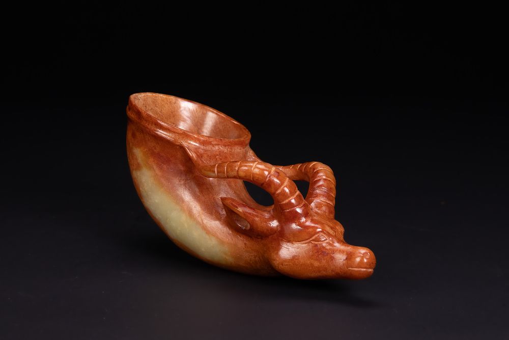 Lot 197: A CHINESE CARVED RUSSET AND CELADON JADE ARCHAISTIC ANIMAL HEADED RHYTON.
