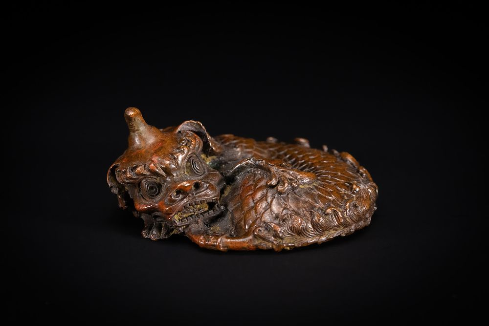 Lot 232: A CHINESE BRONZE PAPERWEIGHT OF A COILED MYTHICAL BEAST.