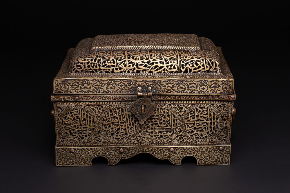 Lot 240: A QAJAR BRASS PIERCED AND ENGRAVED LIDDED QUR’AN HOLDER WITH CALLIGRAPHIC PANELS.
