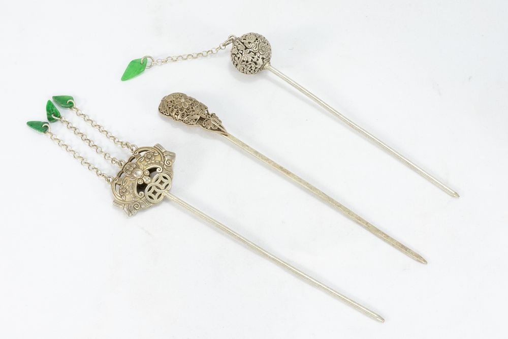 Lot 316: A LOT OF THREE CHINESE-TIBETAN WHITE METAL HAIR STICKS WITH GREEN JADE-COLOURED TASSELS.