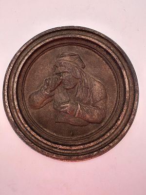 מדליון מתכת תבליט עם דמות מריחה טבק.