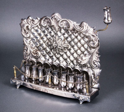 חנוכייה נאה מכסף, גרמניה, סוף המאה ה-19. הלוח האחורי רקוע, חקוק ומוטבע במוטיבים פרחוניים ודוגמת 