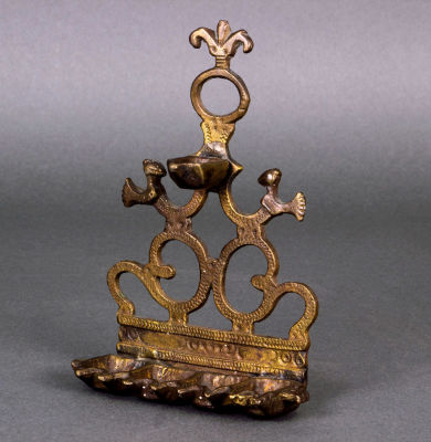 חנוכיית פליז, מרוקו, המאה ה-18/19. הלוח האחורי יצוק וחקוק בצורת קרטוש עם ציפורים ושריגים ומקדימה 