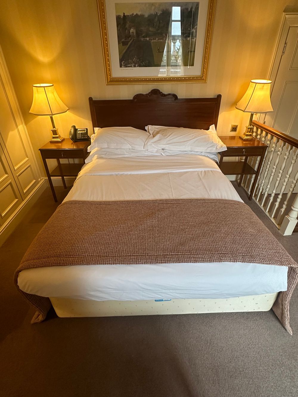 Lot 1709: A Georgian/Victorian Revival Style Bedroom Ensemble, comprising a Dark Wood Headboard for a 150 x 200cm Bed, A Pair of Matching Bedside Tables, A Pair of Brass-Toned Table Lamps, and a Framed Landscape Painting