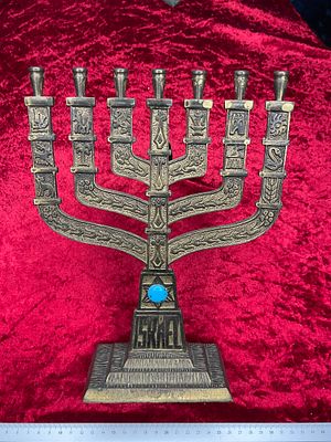 חנוכייה ממתכת בת שבעה קנים מעוטרת בתבליטים וסמלים בסגנון חנוכה מסורתי.
