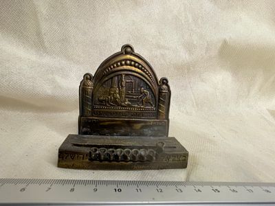 חנוכייה דקורטיבית וינטג’ עם תבליט. פריט מתכתי קטן עם סצנה מובלטת וכיתובים בעברית ובאנגלית 