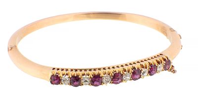 A LATE 19TH CENTURY 18CT GOLD, DIAMOND AND RUBY BANGLE with hinged clasp and safety chain, set 
