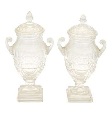 A PAIR OF REGENCY CUT GLASS LIDDED URNS with scolled side handles and raised on square platform 