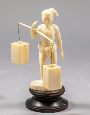 פיגורה יפנית מגולפת בדמות גבר נושא דליי מים על כתפו, ניצב על בסיס עץ. גובה (ללא הבסיס): 11.5 ס"מ.