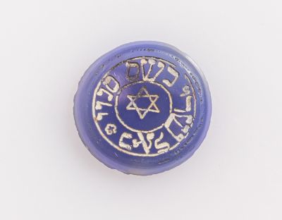 קמע יהודי, אבן כחולה. קמע יהודי לשמירה על היולדת והילוד. אבן כחולה עגולה מעוטרת בחריטה מגן דוד 